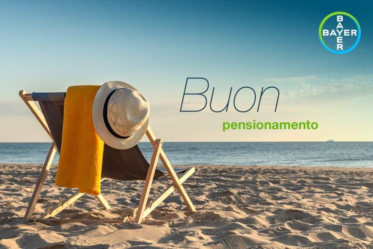 Beach chair with a yellow towel and hat on a sandy shore, ocean and horizon in the background, with "Buon pensionamento" text and Bayer logo in the corner.
