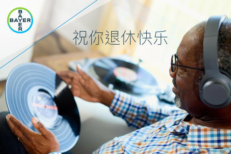 An elderly man wearing headphones holds a vinyl record. A Bayer logo is on the image, along with Chinese text wishing happiness in retirement.