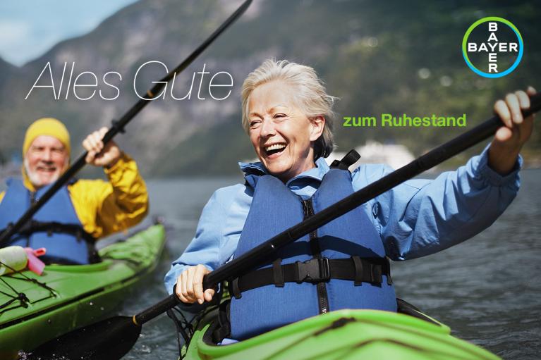 Two older adults kayaking on a lake, smiling. The text reads "Alles Gute zum Ruhestand" with a Bayer logo in the corner.
