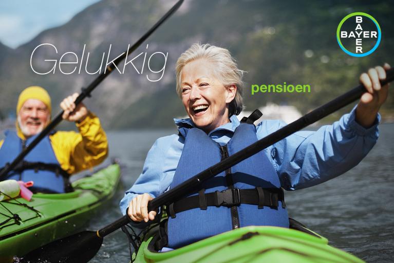 Two smiling older adults kayaking on a lake, wearing life jackets. The background features mountains and text reads "Gelukkig pensioen". Bayer logo is visible.