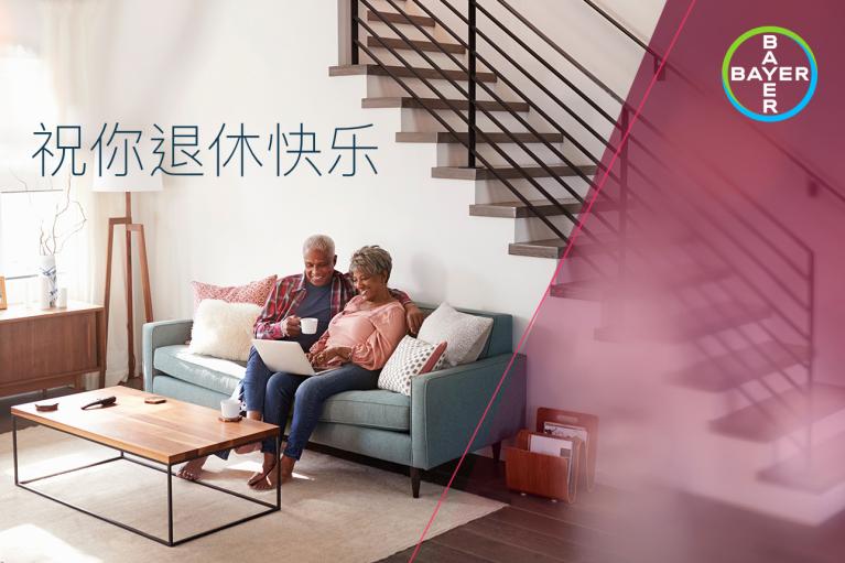 An elderly couple sits on a couch with a laptop. The background shows a modern interior with a staircase. Chinese text and the Bayer logo are visible.