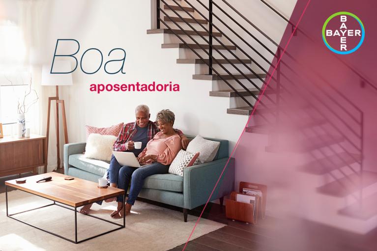 An older couple sits on a couch with a laptop, smiling. The words "Boa aposentadoria" and a Bayer logo appear on the right.