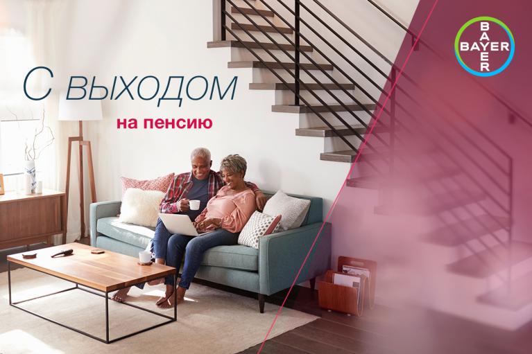 An elderly couple sits on a couch using a laptop under a stairway. Red text in Russian translates to "With retirement." A Bayer logo is in the top right corner.