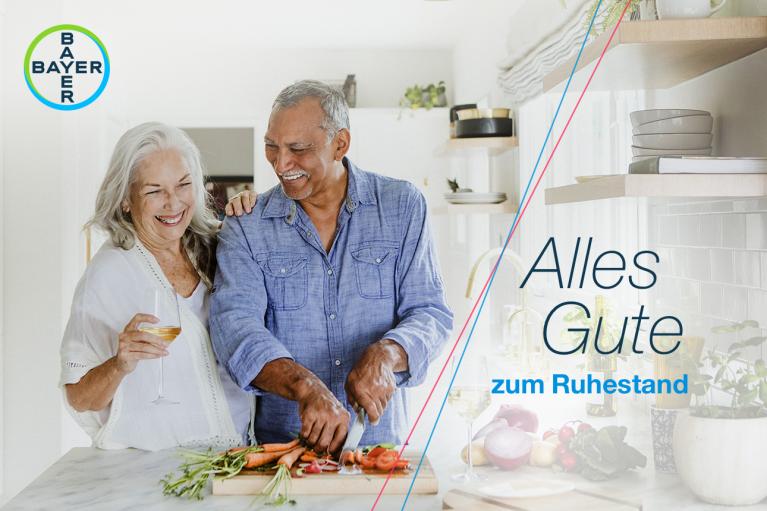 Smiling older couple in a kitchen, preparing vegetables, with "Alles Gute zum Ruhestand" text and Bayer logo.