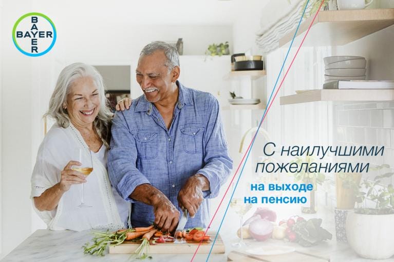 An elderly couple smiles while preparing vegetables in a kitchen. A glass of wine is on the counter. Russian text translates to "With best wishes for your retirement." Bayer logo is in the corner.