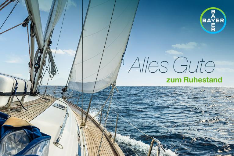 Sailboat on the ocean with the Bayer logo and German text "Alles Gute zum Ruhestand" on a clear day.