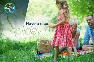 A family has a picnic on a grassy field with the words "Have a nice holiday" and a Bayer logo visible in the image.