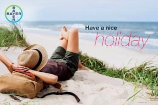 Person relaxing on a sandy beach with a straw hat and a backpack. Text reads, "Have a nice holiday." Bayer logo in the corner.