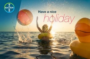 Person in water with inflatable rings and a beach ball during sunset. Text reads "Have a nice holiday." Bayer logo is in the top left corner.