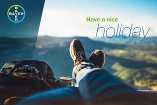 Person relaxing with legs outstretched, overlooking a scenic view with a camera and bag nearby. Text on image reads "Have a nice holiday." Bayer logo in the corner.