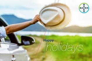 A person in a car holds a white hat out of the window, with a scenic background. Text reads: "Happy holidays." Bayer logo in the corner.