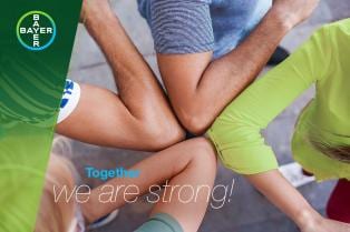 Four people link arms in a supportive circle, with the words "Together we are strong!" displayed. The Bayer logo is visible in the corner.