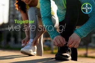 Two people in activewear tie their shoelaces. The text reads "Together we are strong!" and includes the Bayer logo.
