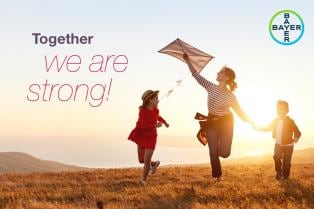 A woman and two children fly a kite on a grassy hill at sunset, with the words "Together we are strong!" and the Bayer logo.