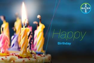 Birthday cake with colorful lit candles on the left, Bayer logo in the top right corner, and the words "Happy Birthday" on the right.