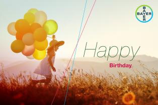 A child running with colorful balloons in a sunlit field, wearing a hat. "Happy Birthday" text and a Bayer logo are on the right.