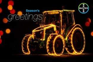 A tractor decorated with festive lights and the text "Season's greetings" alongside the Bayer logo on a black background.
