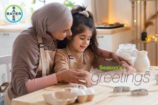 A woman and a child wearing aprons bake together in a kitchen. Text reads "Season's greetings.