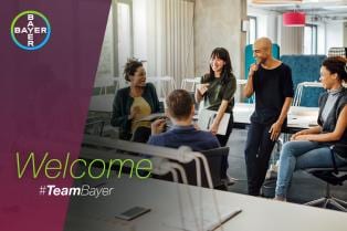 Five people are smiling and talking in an office setting, with a "Welcome #TeamBayer" text overlay and the Bayer logo in the corner.