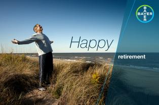Person in a relaxed pose on a coastal path, with the sea in the background and text reading "Happy retirement" alongside Bayer branding.