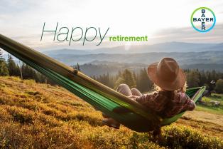 A person wearing a hat relaxes in a hammock overlooking a scenic mountain landscape at sunset. Text reads "Happy retirement." Bayer logo is in the upper right corner.