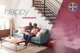 An elderly couple sits on a couch, smiling and looking at a laptop, with "Happy Retirement" text and Bayer logo in the image.