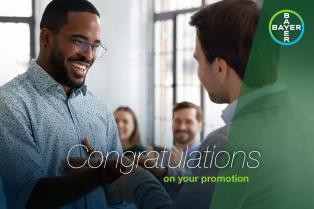 Two colleagues shake hands in an office setting, with the words "Congratulations on your promotion" and a Bayer logo in the corner.